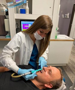 Female dental professional using a polishing tool on a male patient during a dental cleaning.